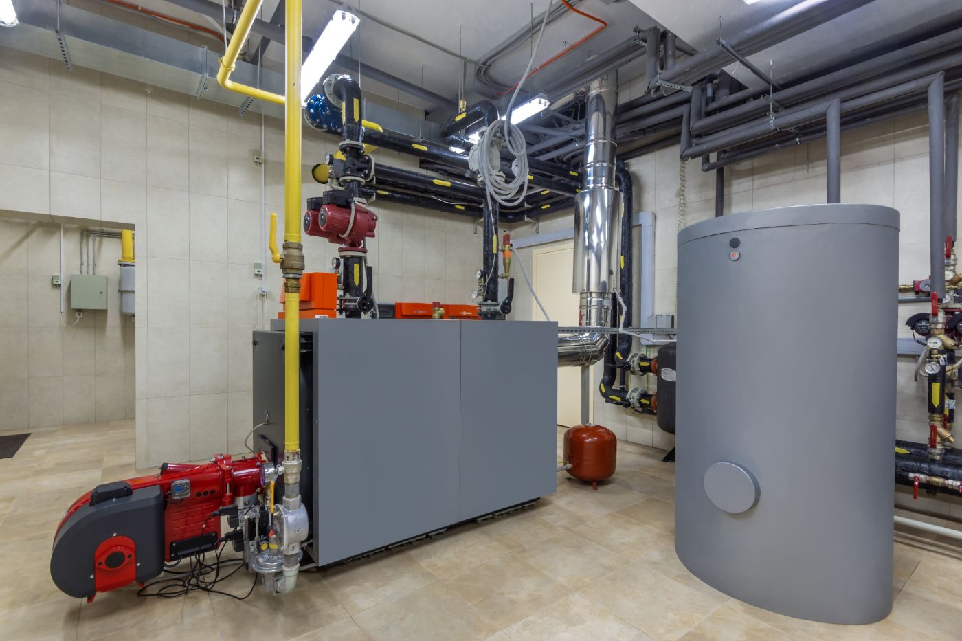 Modern boiler room with industrial heating system, gray tanks, red burner, and overhead piping