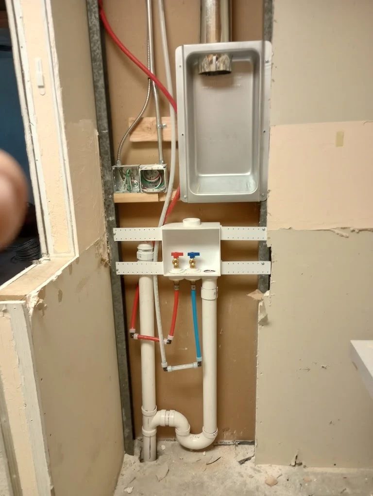 In-wall plumbing installation with white PVC pipes, red and blue supply lines, and shutoff valves during bathroom renovation