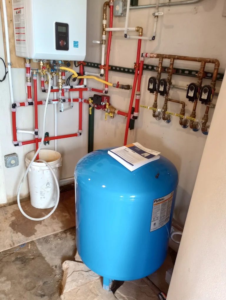 Tankless water heater system with blue pressure tank and red piping installation