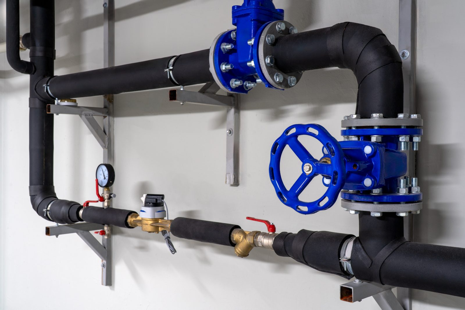 Industrial piping system with blue ball valves and black insulated pipes mounted on wall