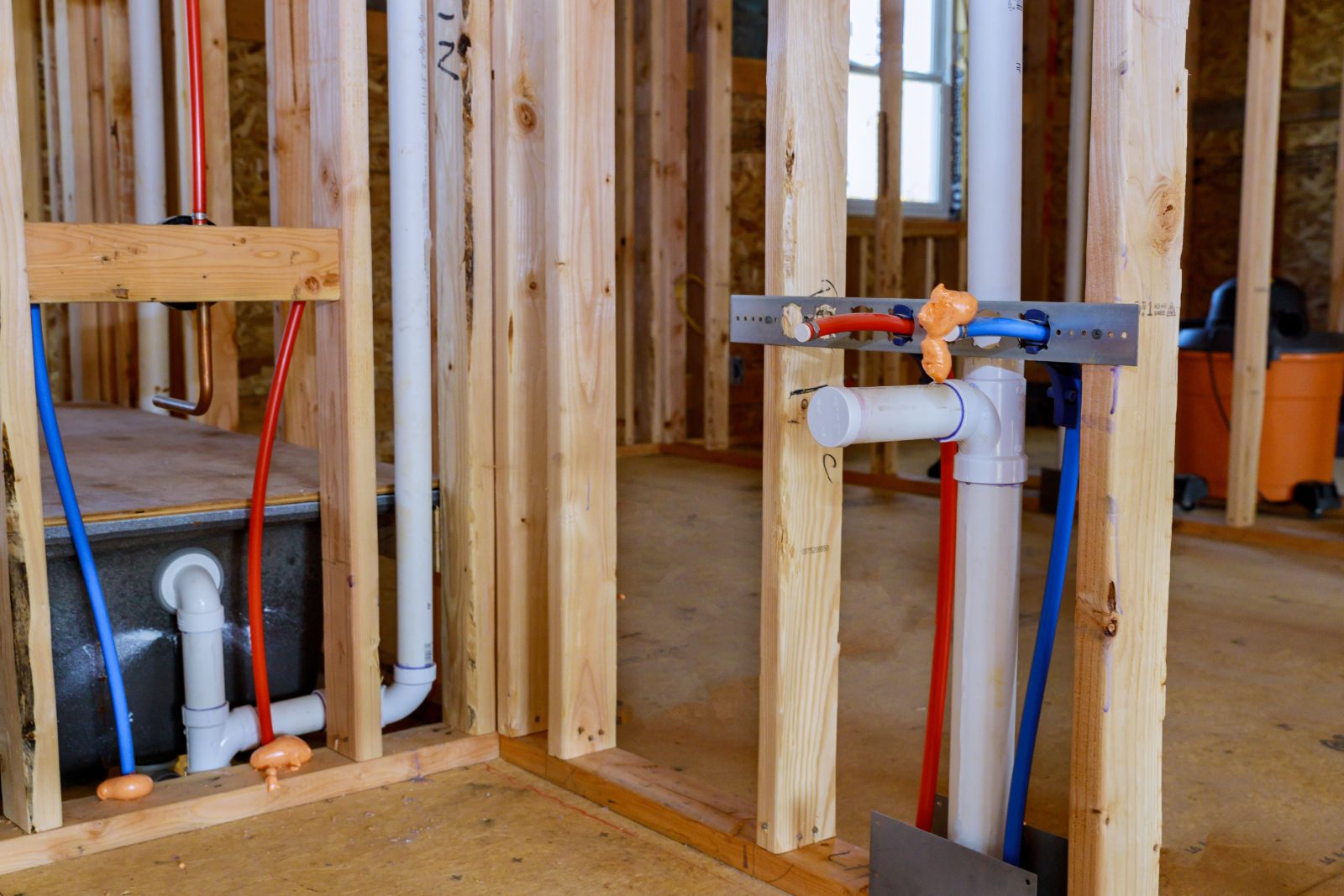New home construction showing framed walls with plumbing pipes and electrical wiring installation