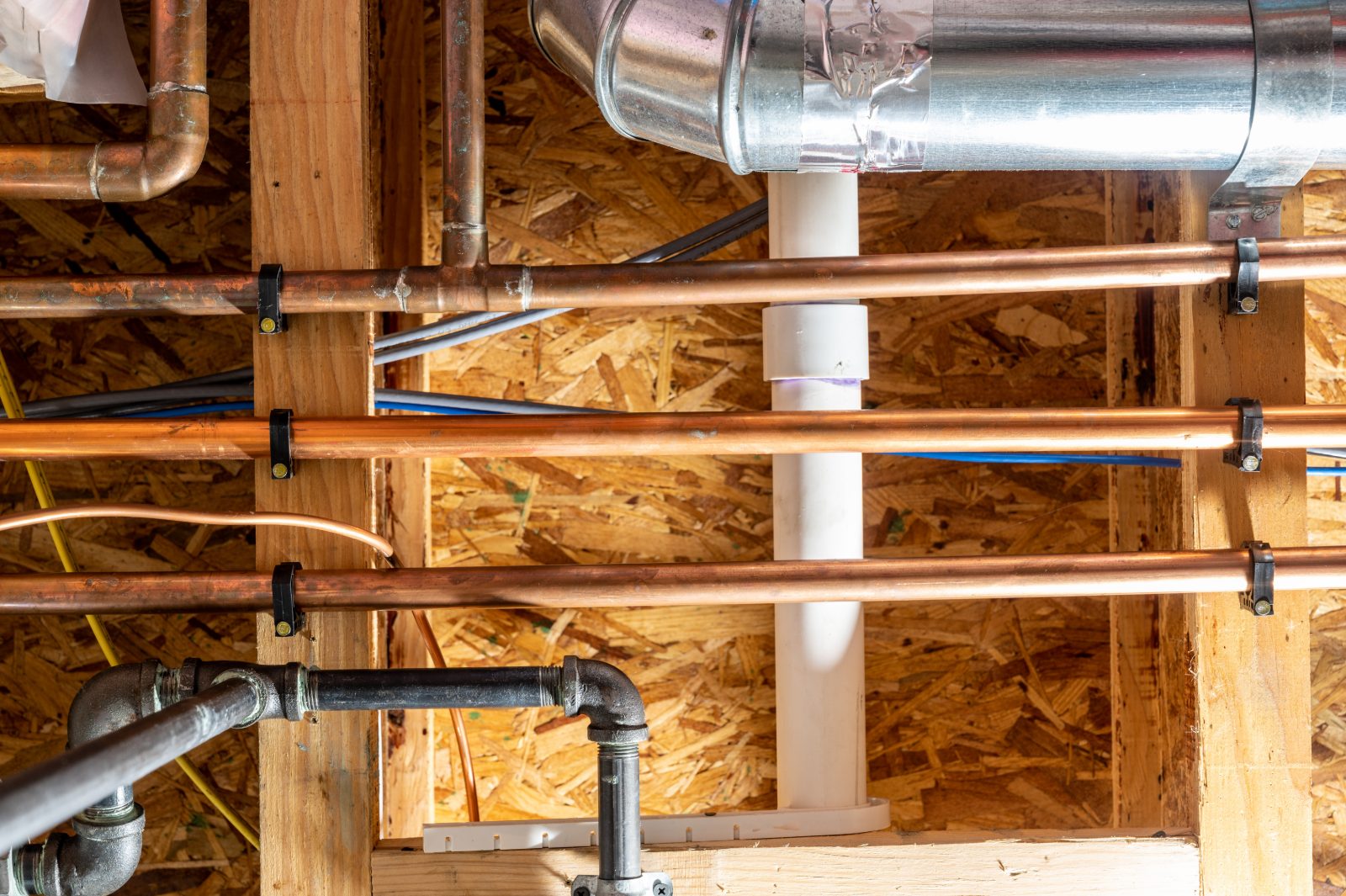 Residential HVAC and plumbing installation in attic framing with copper pipes and ductwork